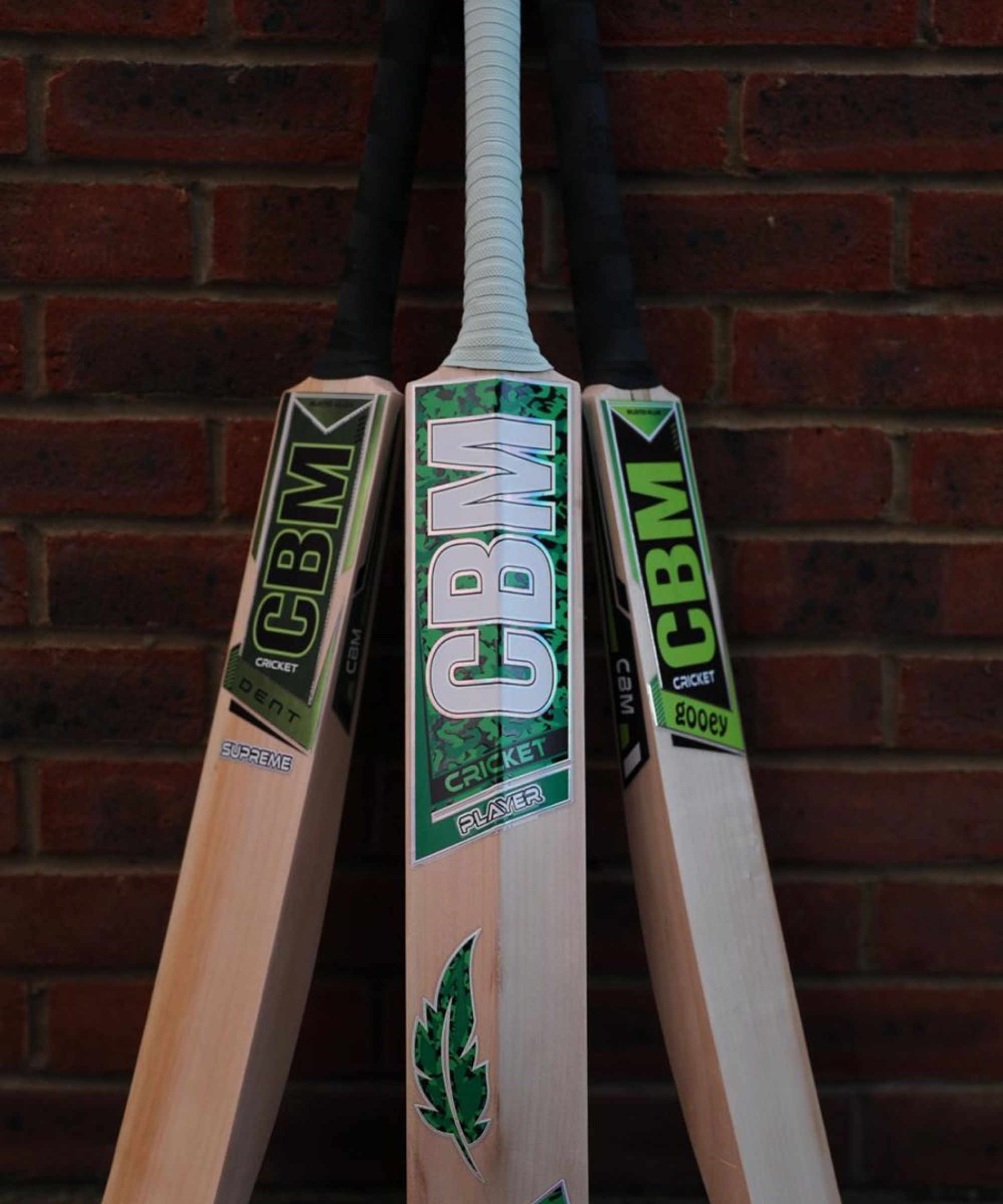A finished CBM cricket bat resting against a workshop wall.